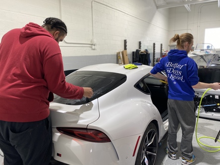 Two restyling workers apply car window tinting in Livonia